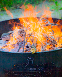The silhouette of a Door County Lighthouse glows as the flames of a fire pit flicker in the dusk.